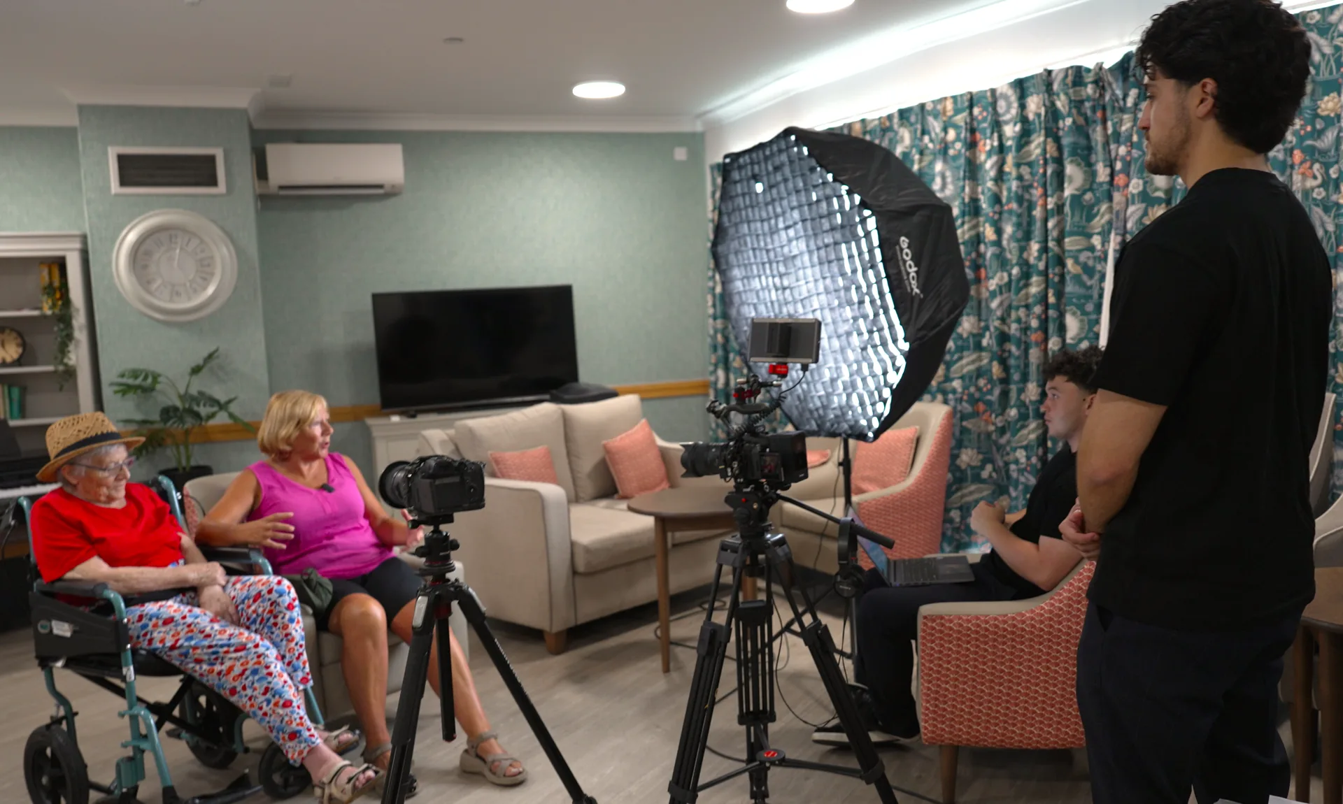 A small crew filming a resident's testimonial in a care home lounge.