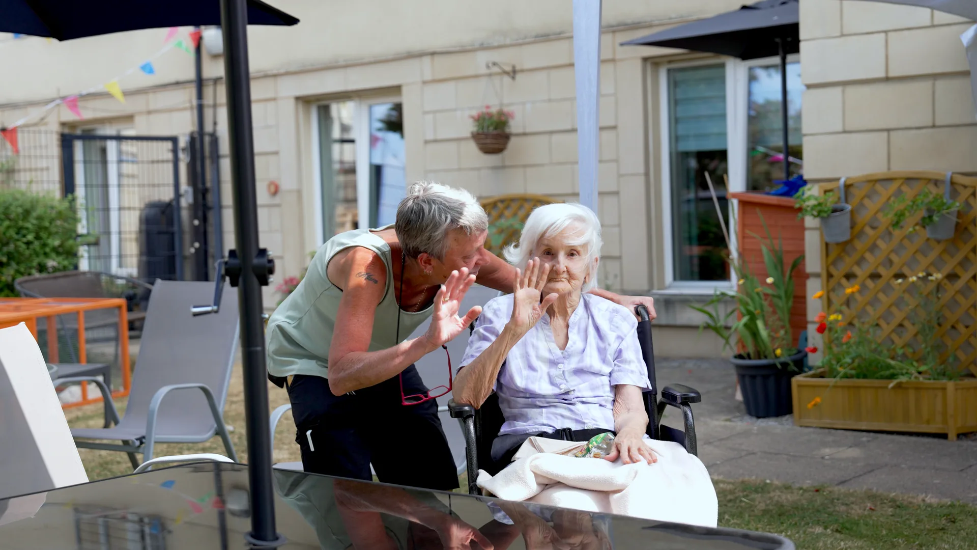 A carer and a resident waving together in the garden.