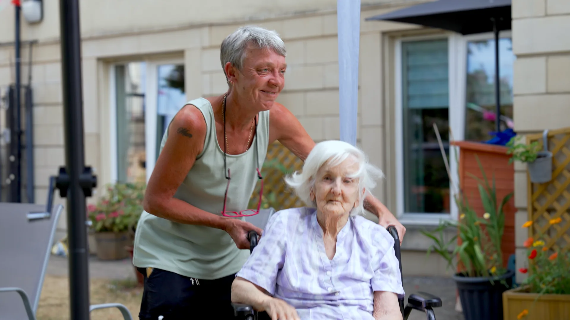 A carer walking with a resident through the garden of a care home.