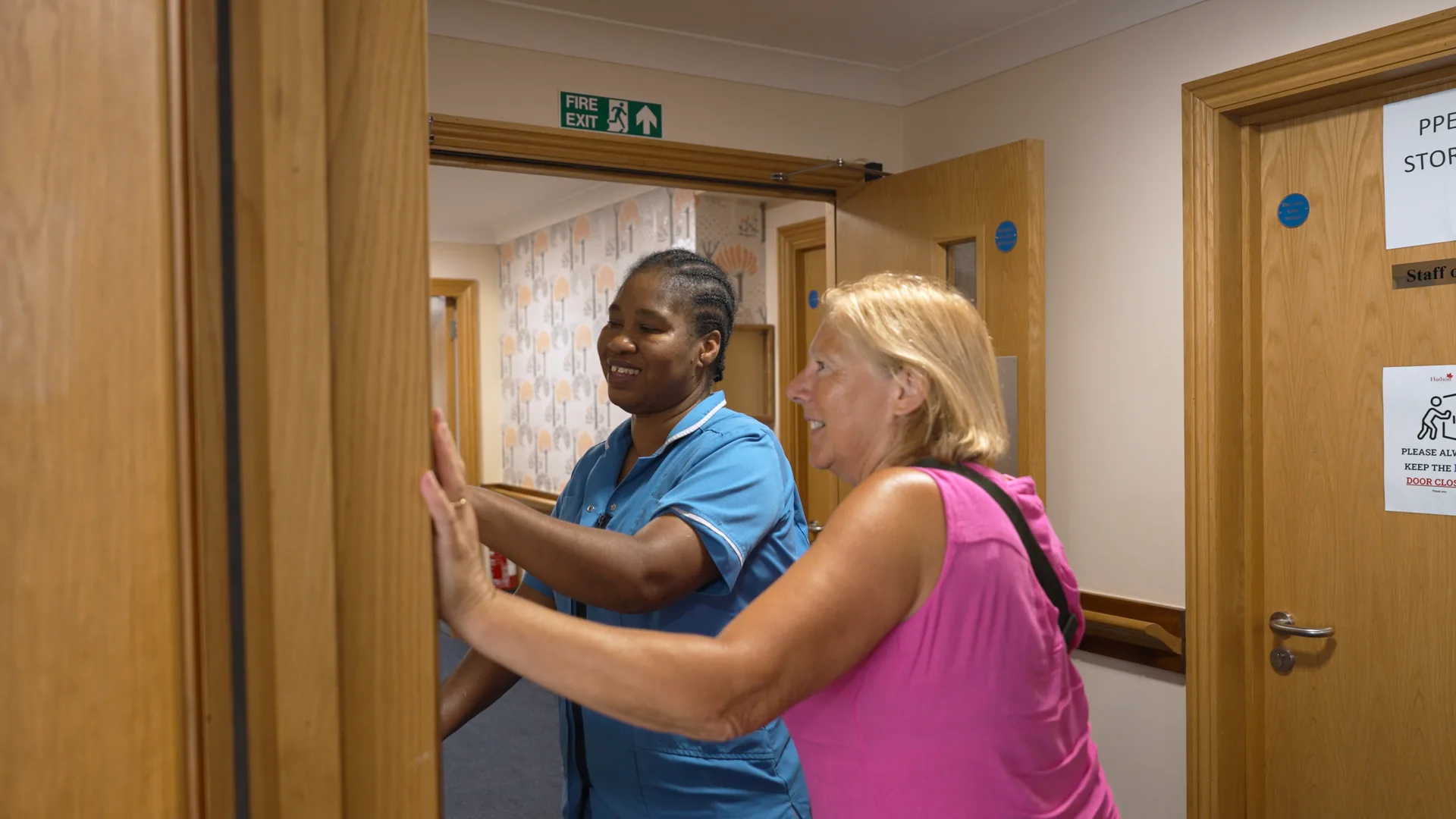 A carer warmly welcoming a visitor at the doorway of a care home.