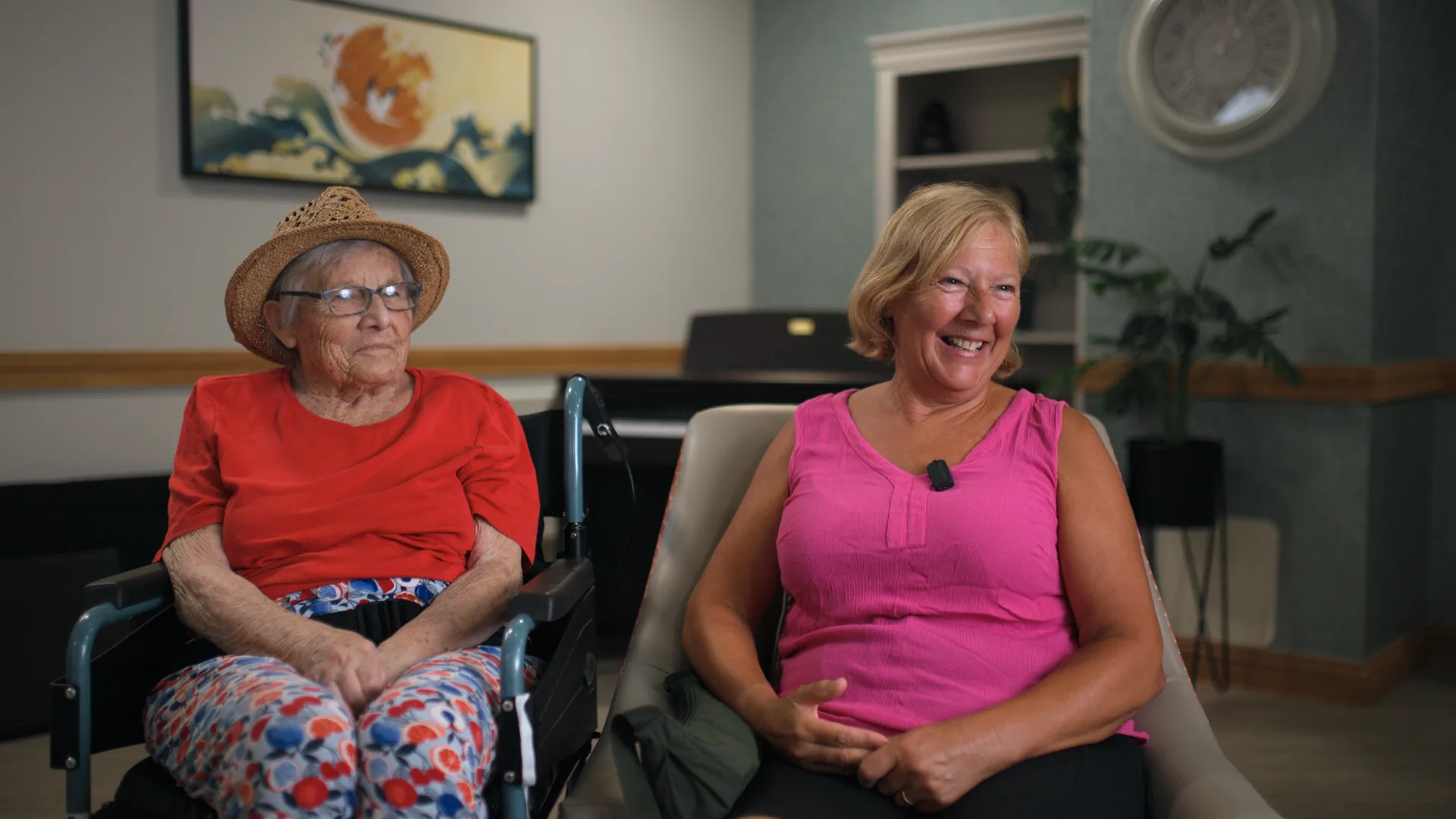 An adult daughter smiling with her mother in a care home lounge.