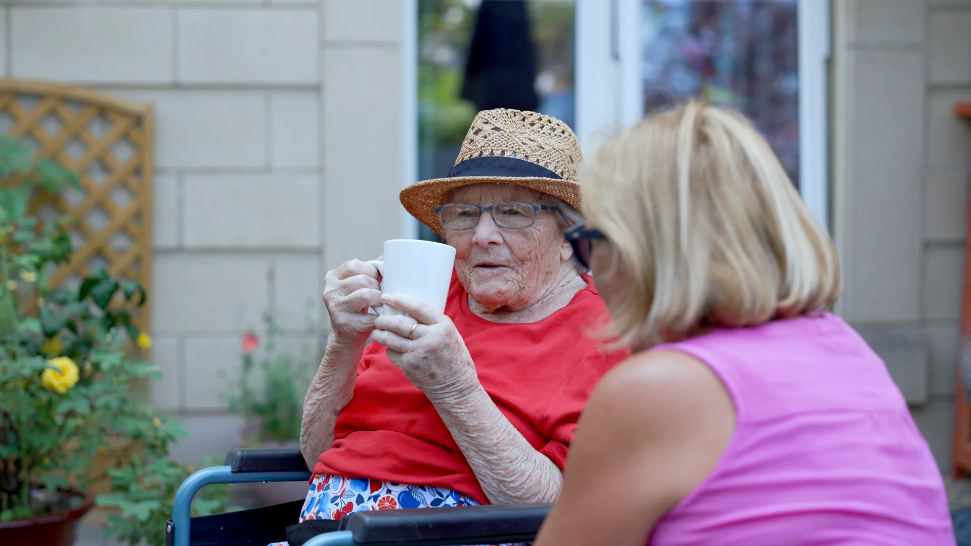 A care home resident having tea in the garden with a visiting family member.