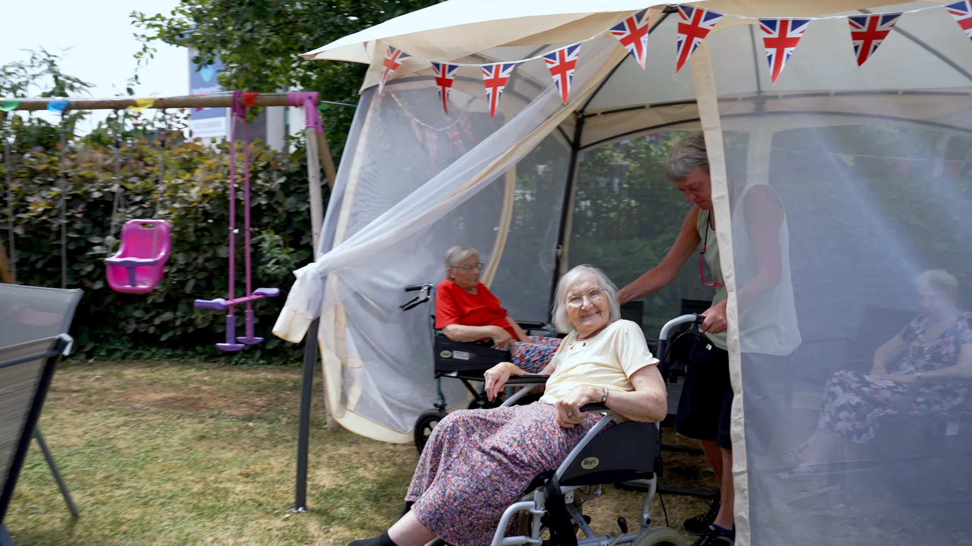 A smiling care home resident with a carer at a garden party.