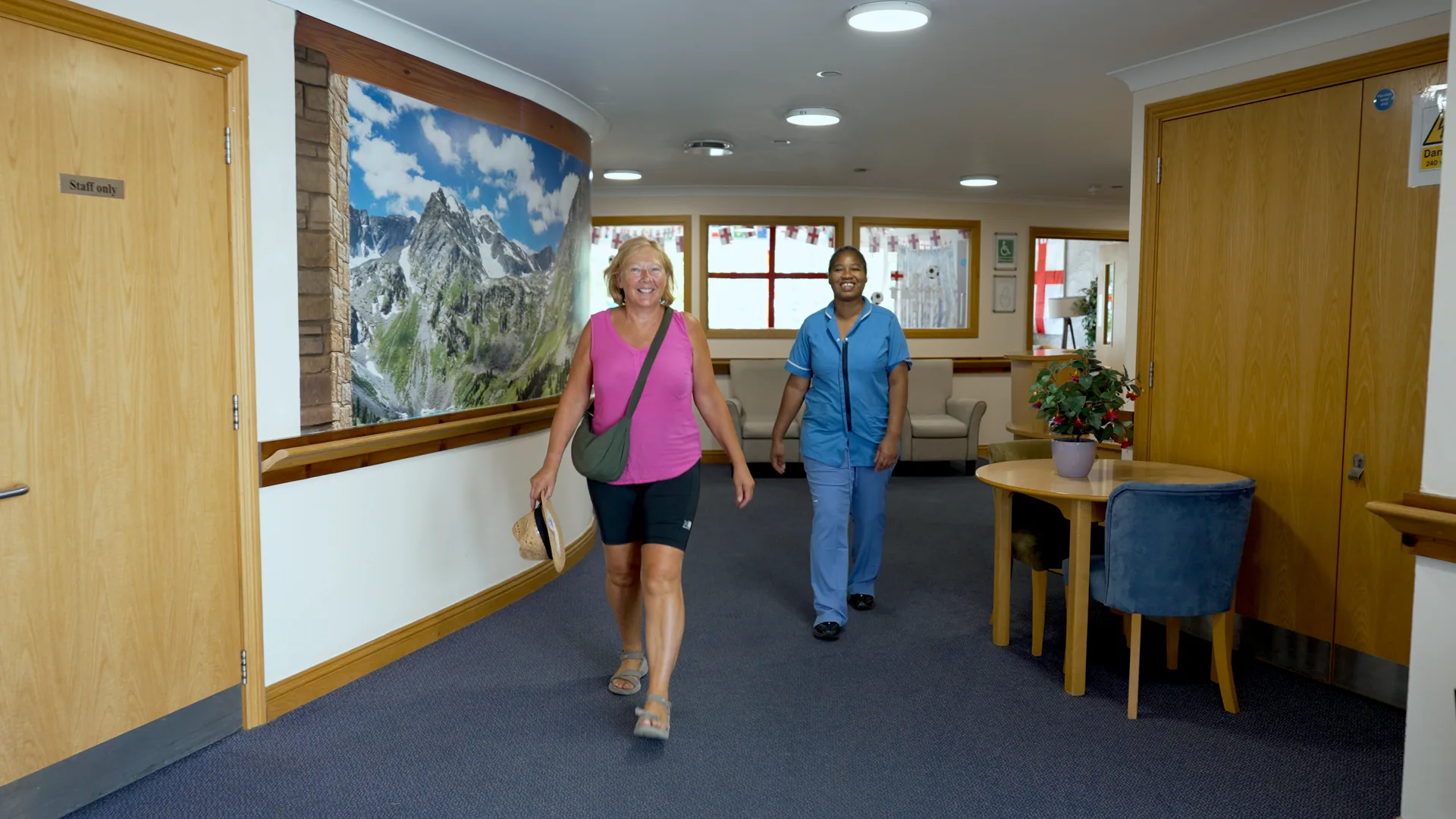A visitor and a carer talking warmly in a care home corridor.
